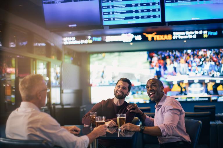 Three friends enjoying drinks while watching sports on multiple TVs