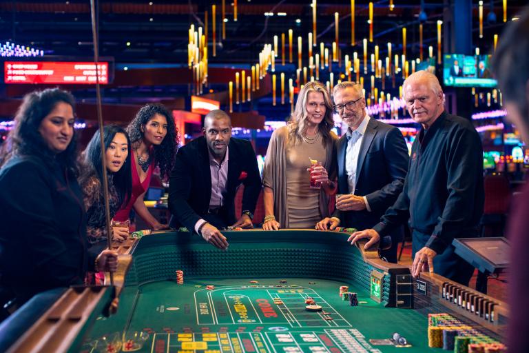 Excited and anxious adults gather around a Craps table awaiting the next roll