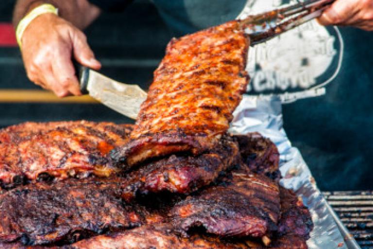 Person preparing a stack of BBQ ribs