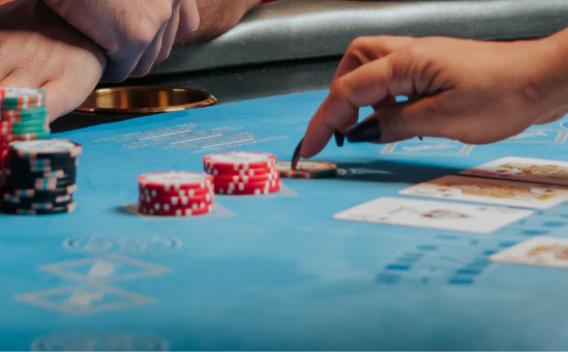 A close-up view of a poker game in action, showing players' hands with cards and chip stacks on a casino table.