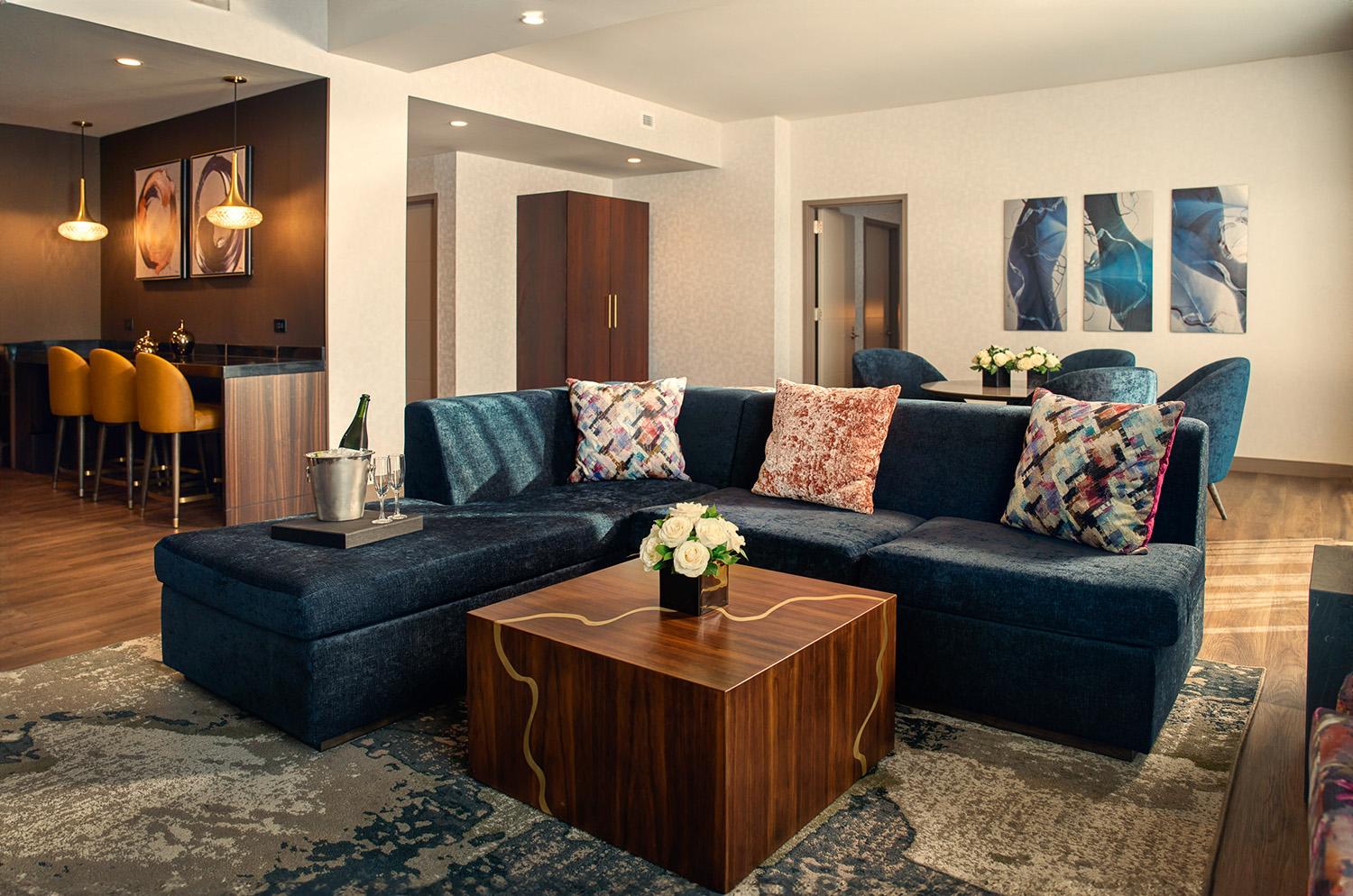 A modern hotel room with a large sectional, reclaimed wood coffee table and bar seating