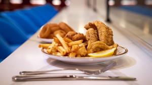 A plate of fried fish and chips with lemon wedge and tartar sauce, placed on a diner counter with blue seating in the background.
