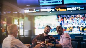 Three friends enjoying drinks while watching sports on multiple TVs