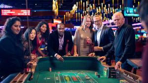 Excited and anxious adults gather around a Craps table awaiting the next roll