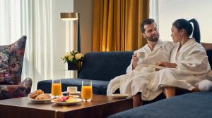 A man and a woman enjoy breakfast and coffee on the couch of their hotel room