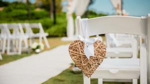 A rustic heart decoration hangs from the back of a white folding chair, in the background an altar can be seen