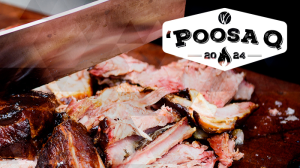 Closeup of BBQ meat being chopped up on a cutting board behind the Poosa Q logo 