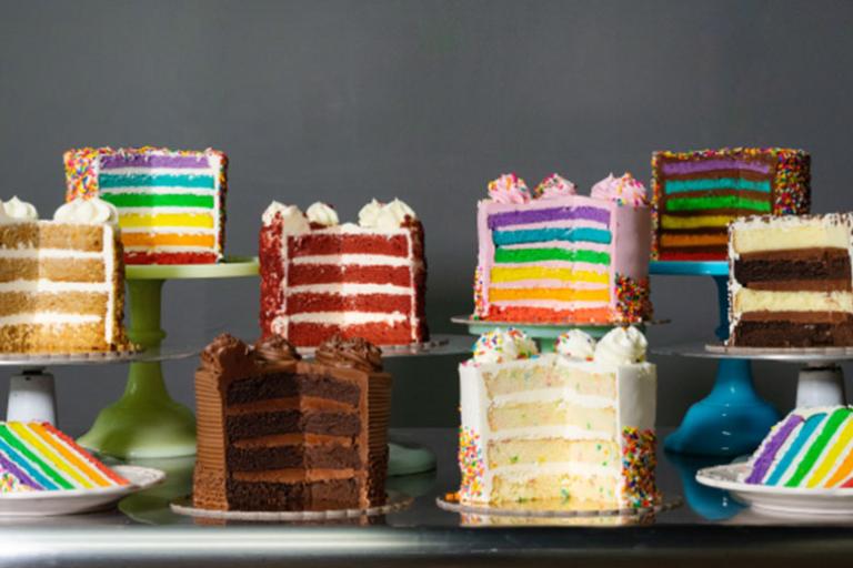 Colorful, layered cakes on assorted cake stands, featuring vibrant decorations and sprinkles.