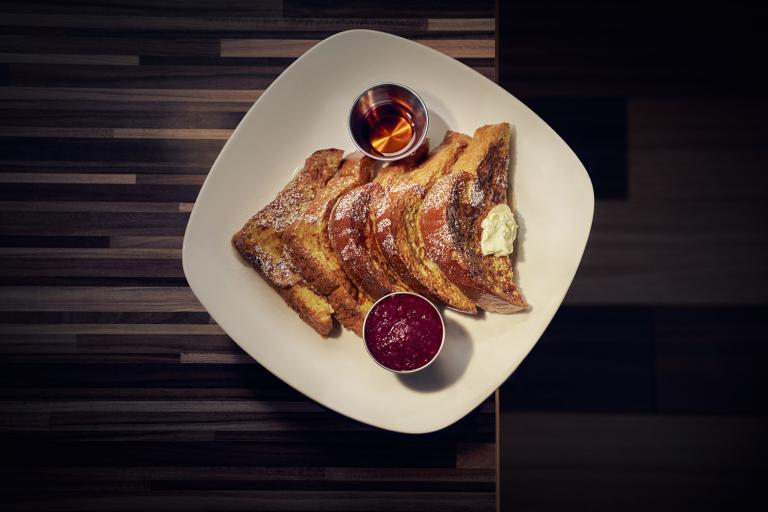A plate of french toast with syrup on a wood table top
