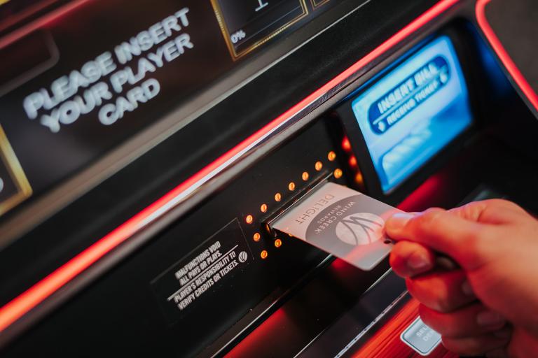 A close-up of a person inserting a loyalty card into a slot on a vibrant, illuminated arcade game machine, with prompts and digital screens visible.
