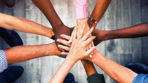 A diverse group of hands stacked together in a symbol of teamwork and unity, shot from above against a blurred background.