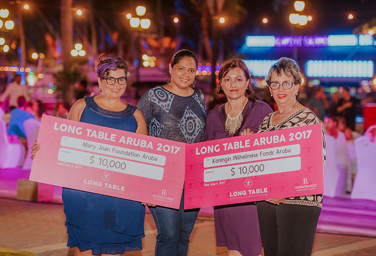 Four women holding large checks from the Wind Creek Aruba Long Table event
