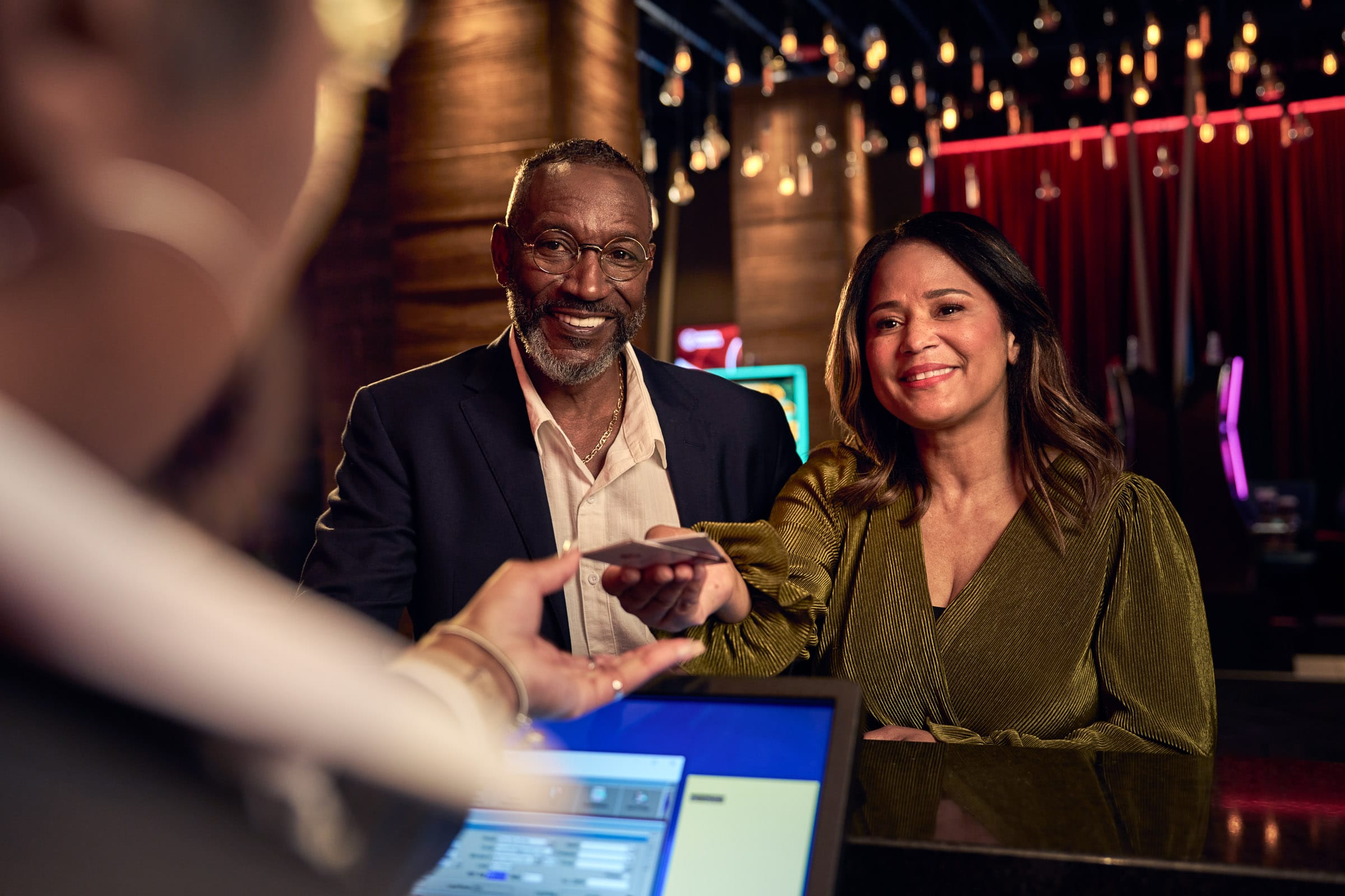 A man and a woman at the hotel desk hand their room keys to an employee behind a desk