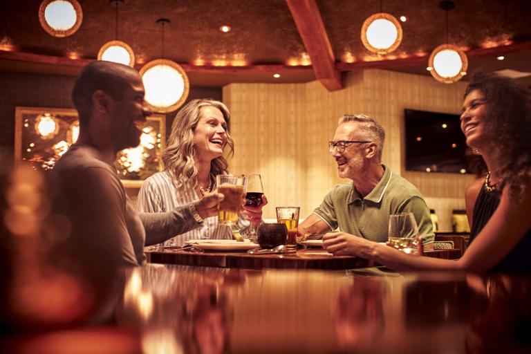 Four friends enjoy drinks and a meal in a warmly lit space