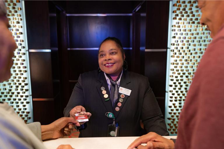 A Wind Creek employee adorned with pins smiling while returning a customer's card