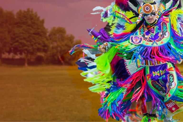 A Poarch Creek person dressed in colorful traditional attire in an open field