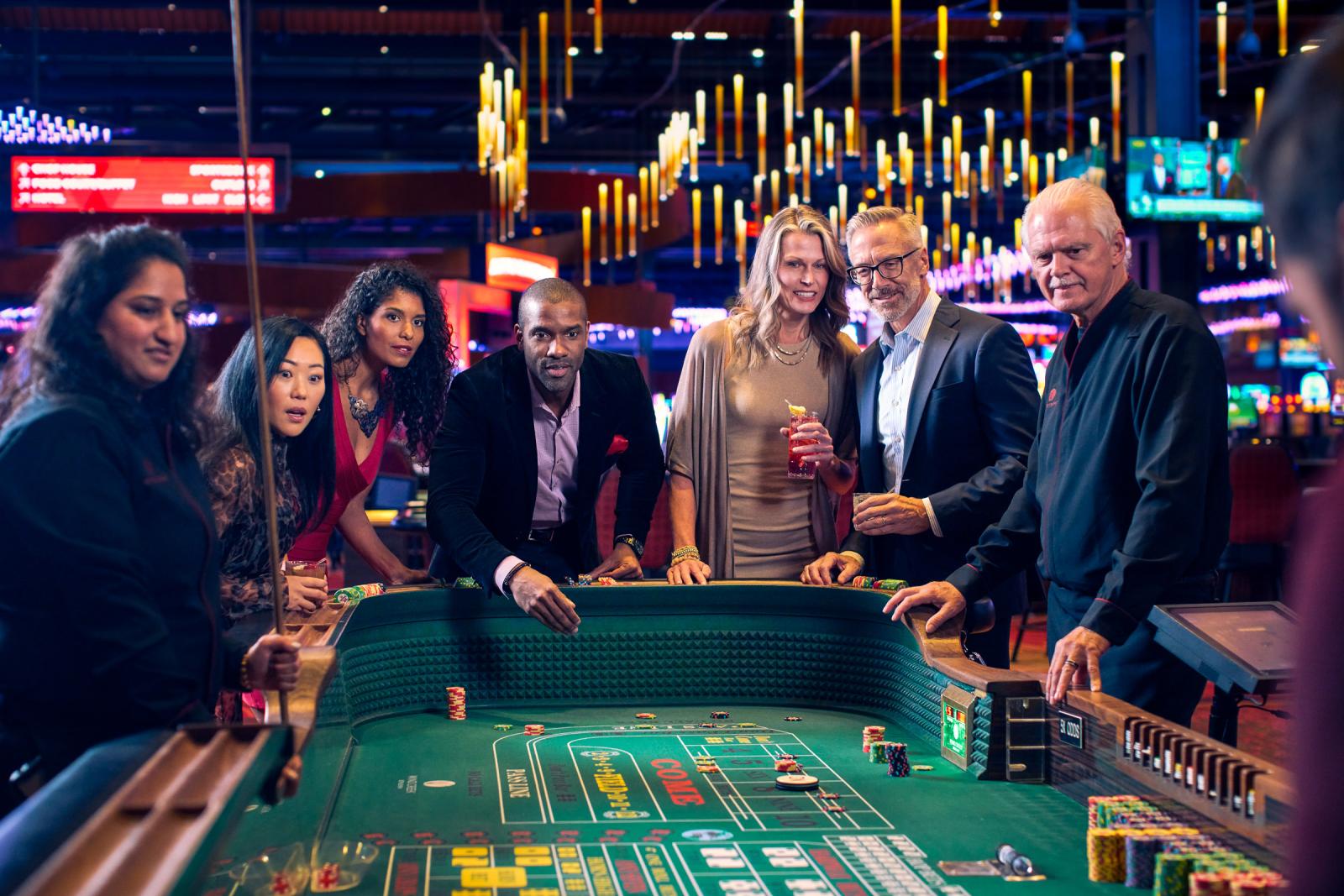 Excited and anxious adults gather around a Craps table awaiting the next roll