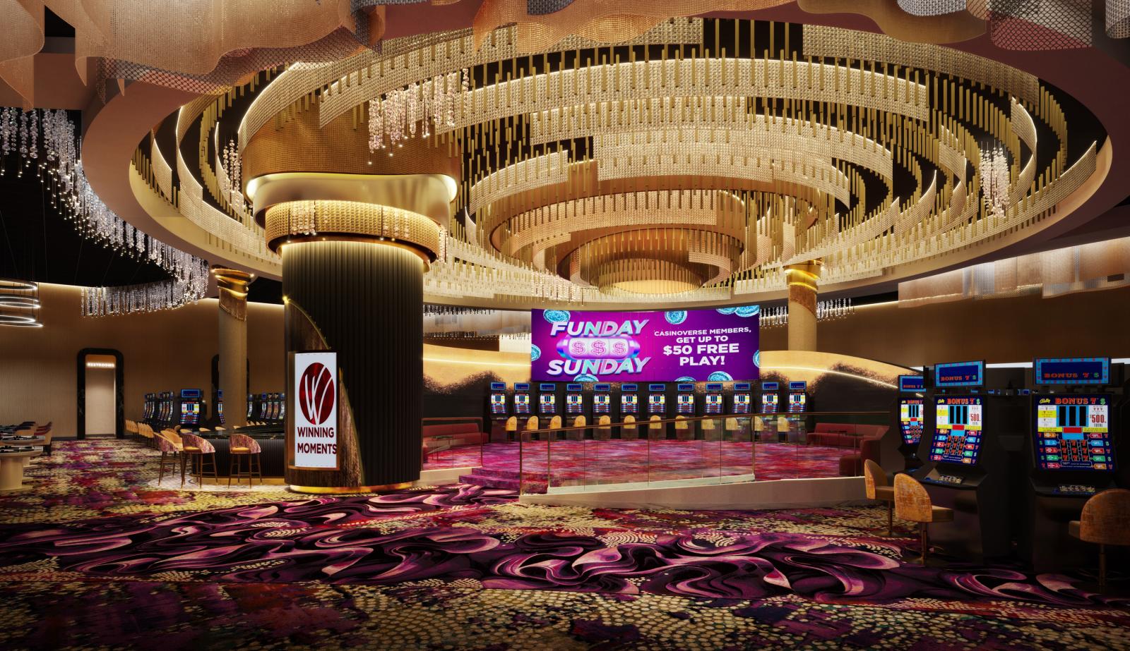 View of an open area on the casino floor with a wall-sized screen displaying a current promotion and a circular hanging lighting installation 