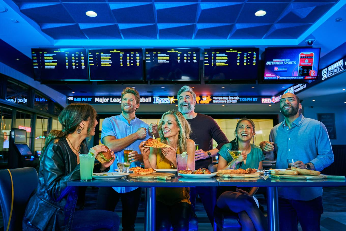 Friends enjoying Pizza and drinks while watching sports on multiple TVs