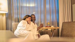 A couple wearing robes sits together by a large window