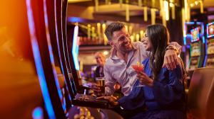 A woman holds a cocktail and laughs while playing a slot machine