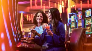 Two women enjoy cocktails and play a slot machine