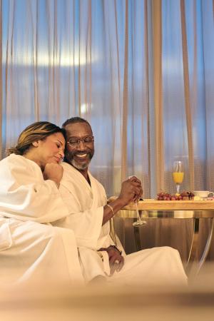 A couple wearing robes sits together by a large window